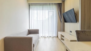 A modern living room with a sofa, a TV mounted on the wall, and a wooden panel design. - New Condo Near Beach Prime Location C228 (Choeng Thale)