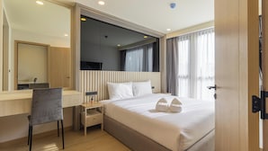 A hotel room with a bed, a desk, a chair, a nightstand, a mirror, and a window with curtains. - New Condo Near Beach Prime Location C228 (Choeng Thale)