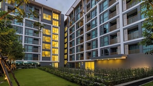 A modern multi-story hotel with balconies, a well-maintained lawn, and a clear sky. - New Condo Near Beach Prime Location C228 (Choeng Thale)