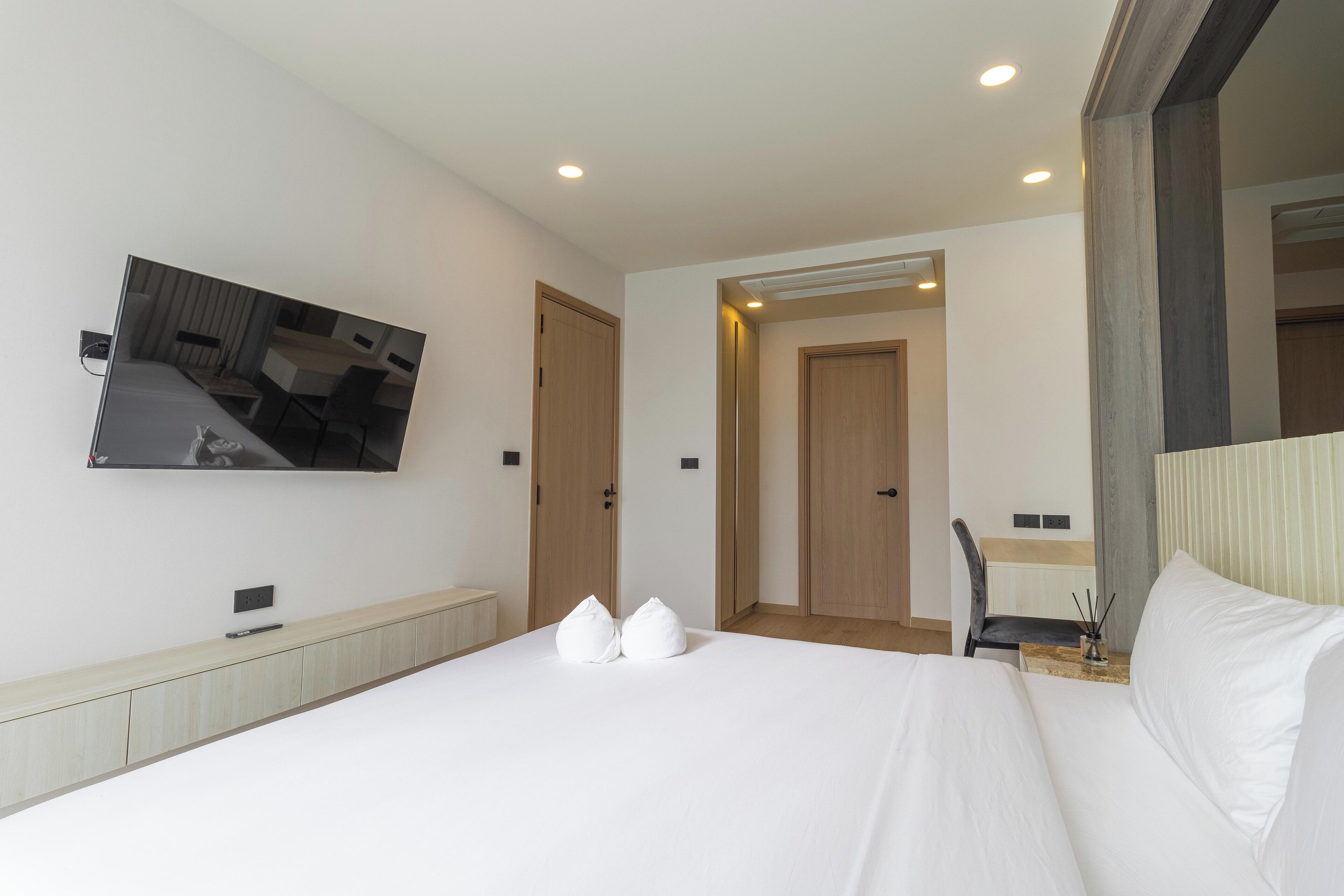 A modern hotel room with a large bed, a flat-screen TV mounted on the wall, and a small desk with a chair.
