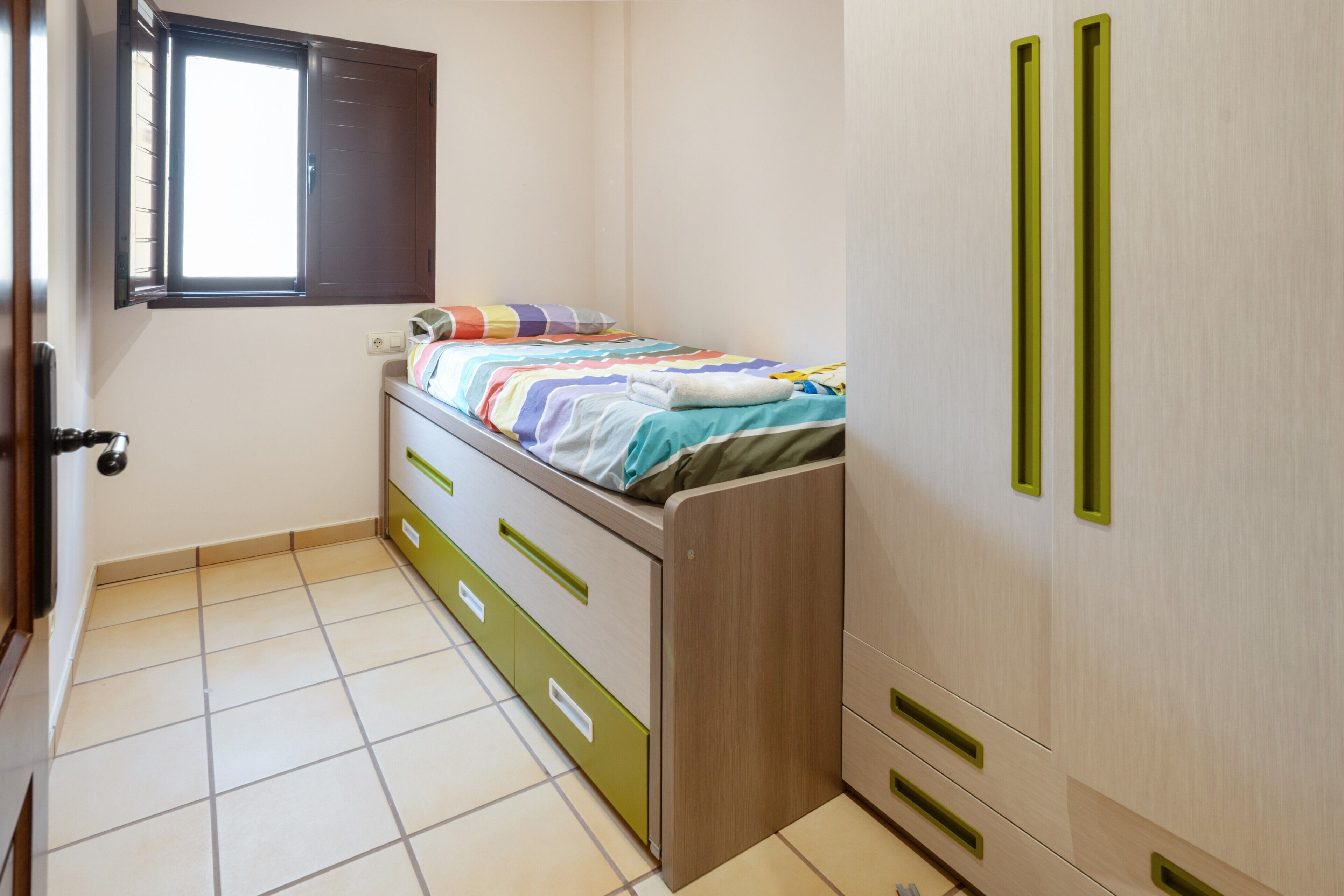 Una camera da letto con un letto, una finestra, un armadio e un pavimento piastrellato.