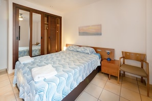 A bedroom with a bed, a nightstand, a chair, a painting on the wall, and a sliding door.