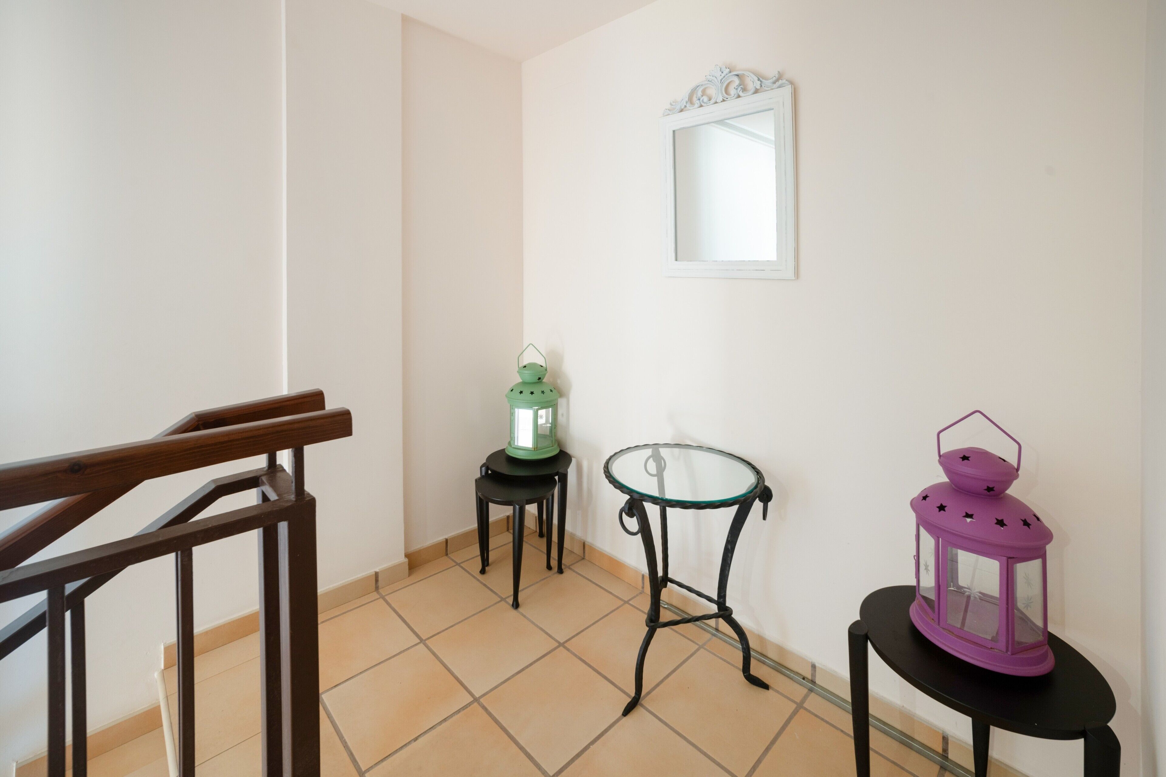 A staircase with wooden handrails, a green lantern, a glass table, and a purple lantern on a small table.
