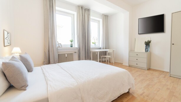 Une chambre à coucher moderne, équipée d’un lit, d’une table de chevet, d’une lampe et d’un téléviseur fixé au mur.