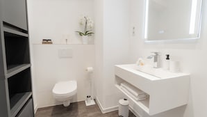 Une salle de bain moderne avec un lavabo blanc, des toilettes et un miroir au-dessus du lavabo.