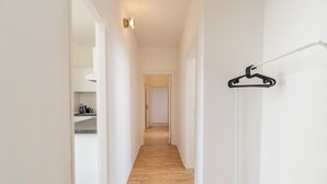 Un couloir étroit avec un plancher en bois, des murs blancs et un portant noir sur un socle blanc.