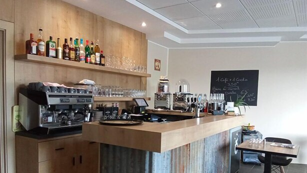 A modern bar area with a wooden counter, espresso machines, and a variety of liquor bottles. - Le commerce d'Ophelie (Corcieux)