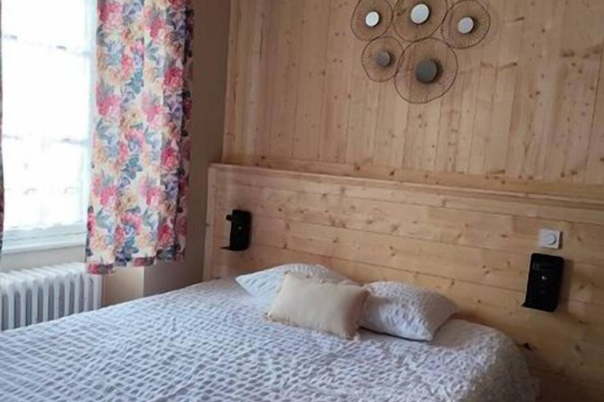 A bedroom with a wooden headboard, a bed with white linens, and a window with floral curtains.