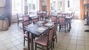 A dining area with multiple tables and chairs, large windows, and a tiled floor. - Le commerce d'Ophelie (Corcieux)