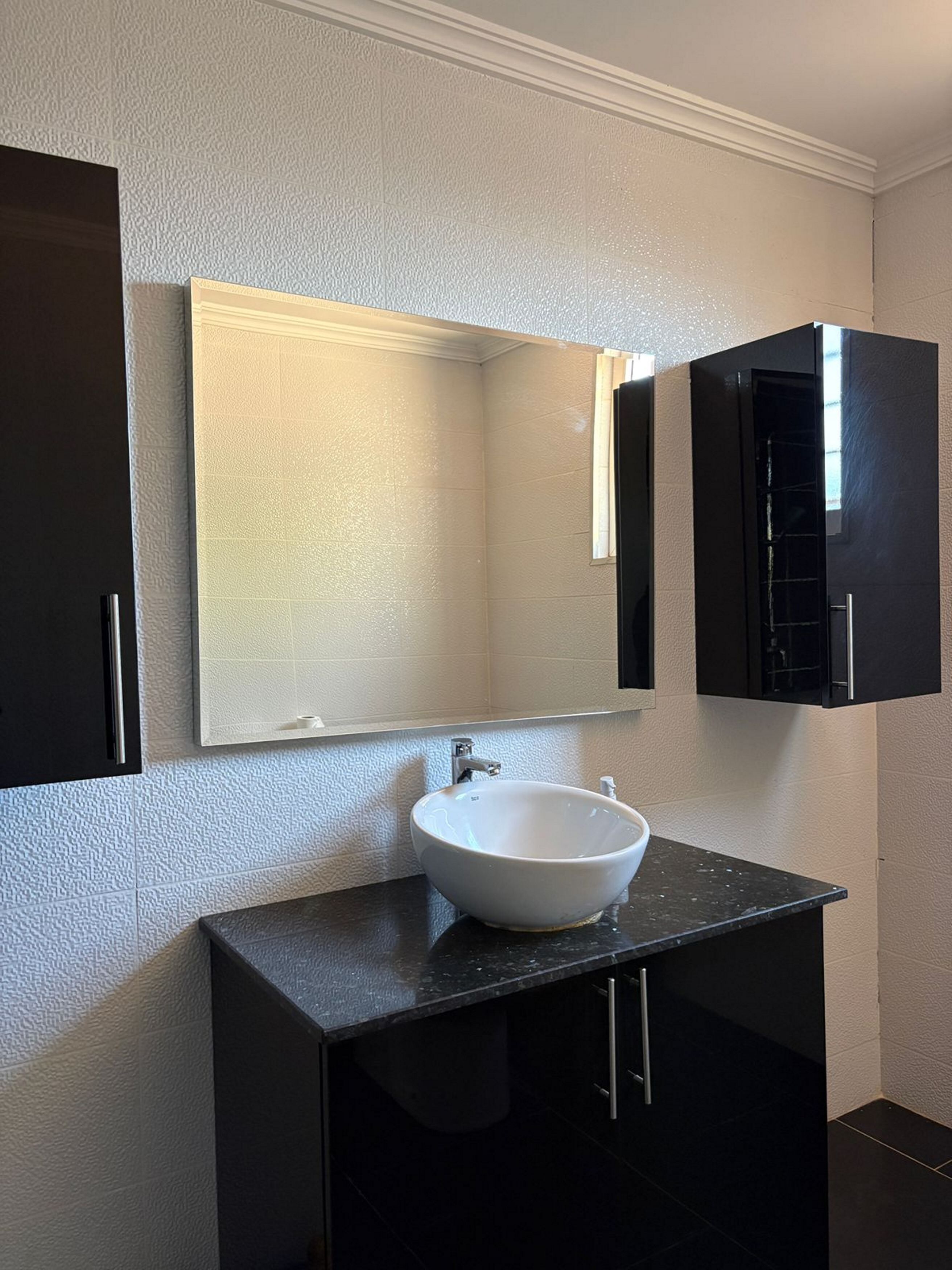A bathroom with a white sink, black cabinets, and a mirror.