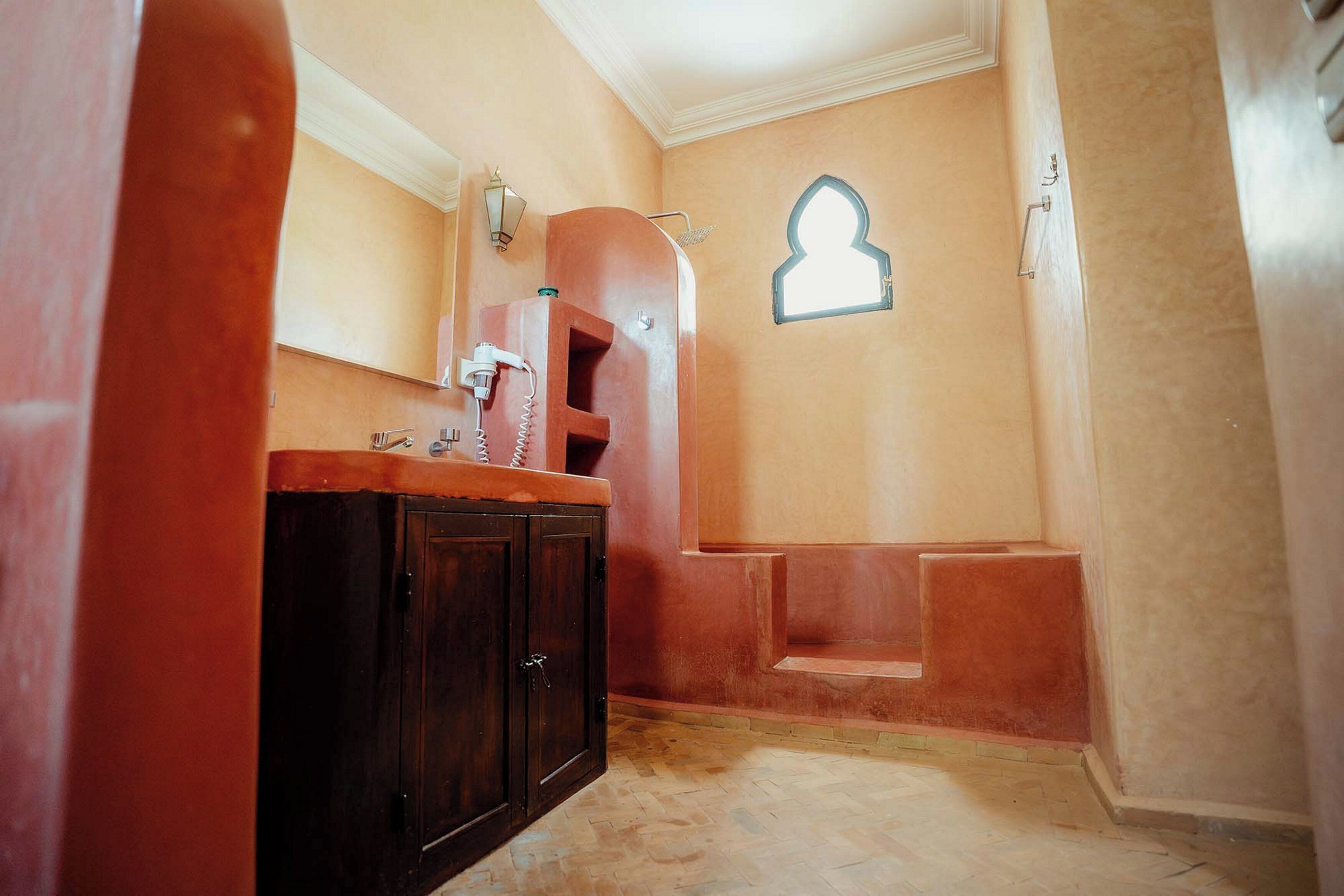Een badkamer met een houten kastje, een wastafel, een douche en een wandlamp.