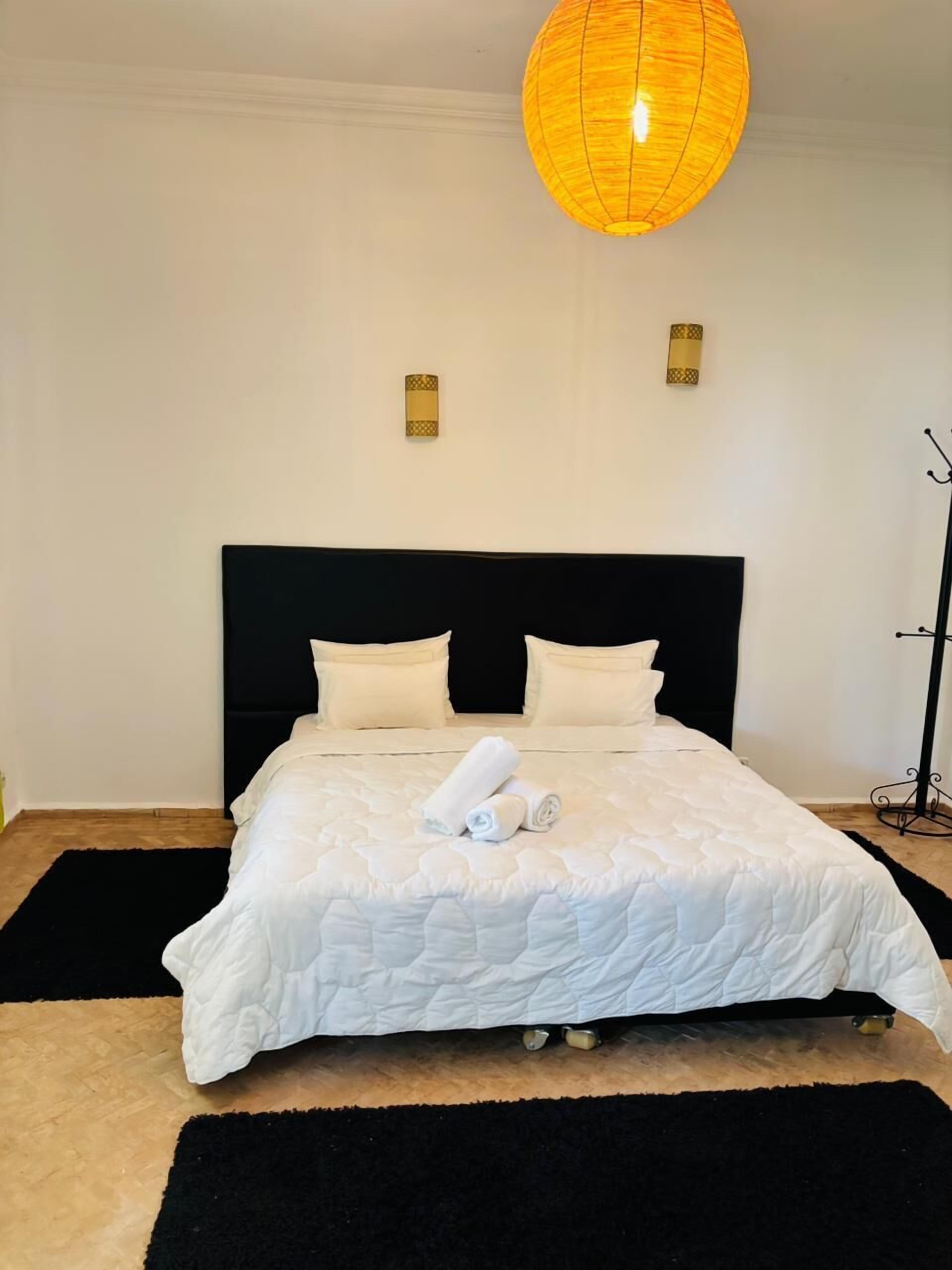 Una cama bien hecha con ropa blanca, un cabecero negro y dos lámparas fijadas a la pared.