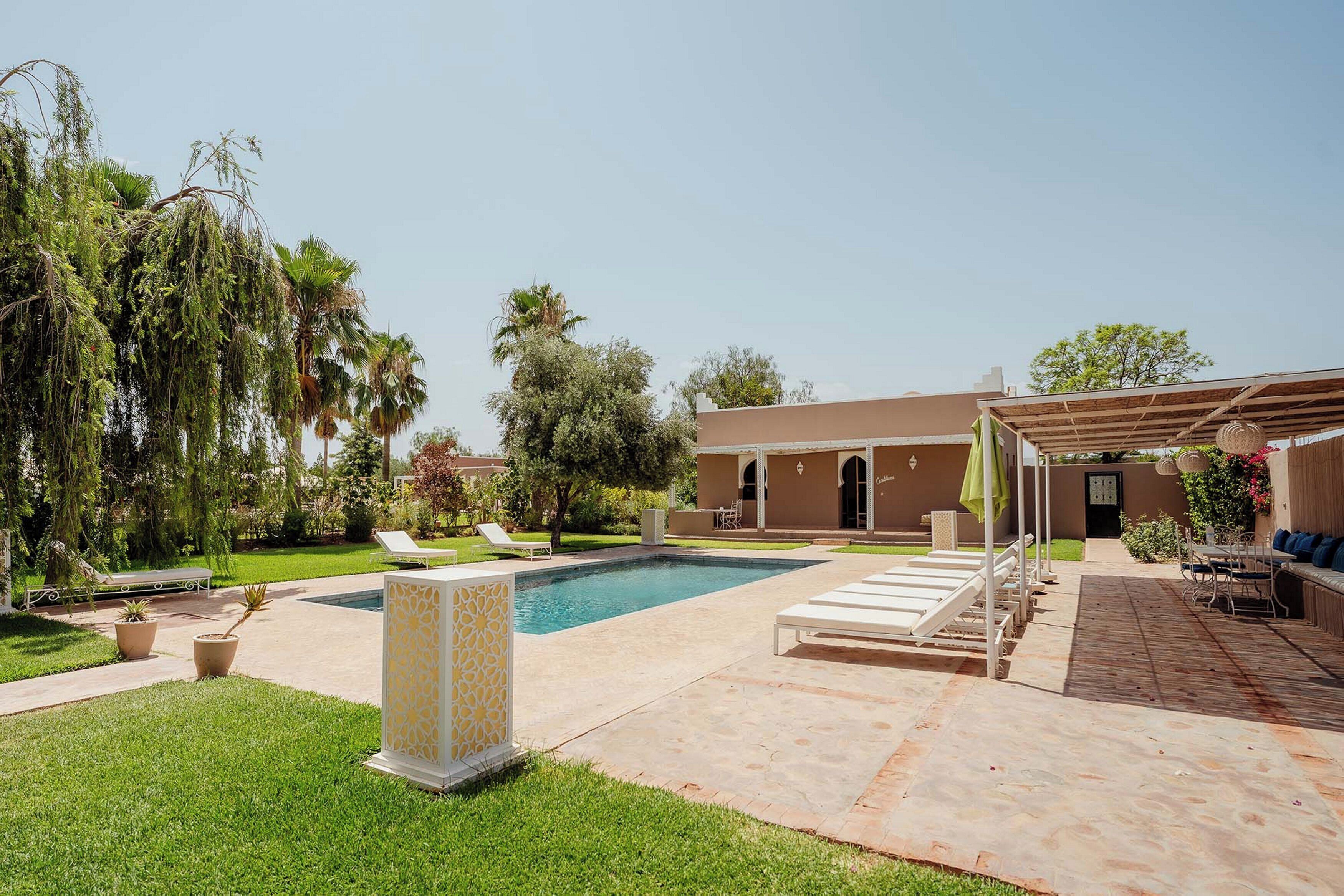 Zona de piscina con sillones de descanso, una pérgola y un edificio con entrada en arco.