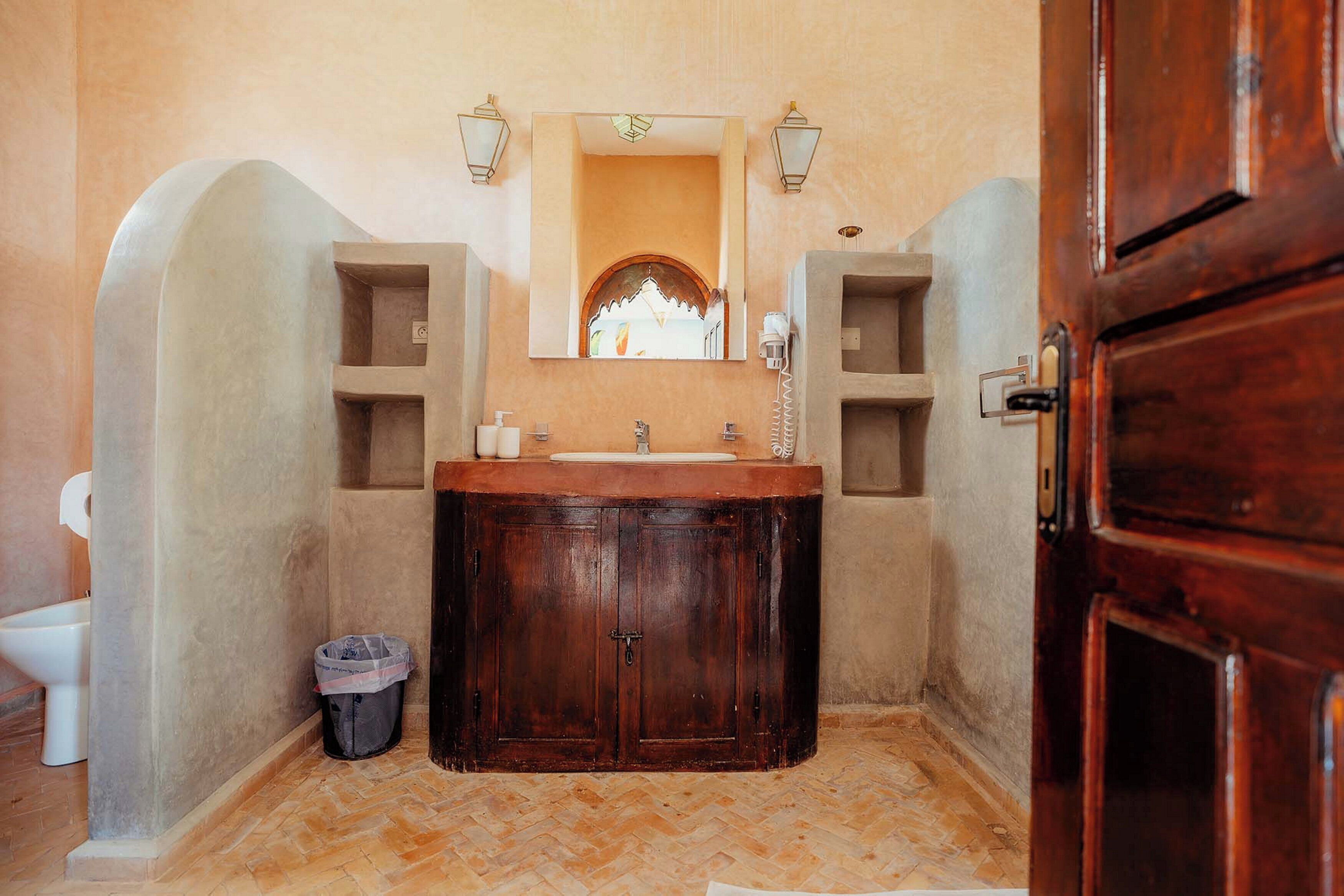 A bathroom with a wooden vanity, a mirror, two wall-mounted lights, and a trash bin.