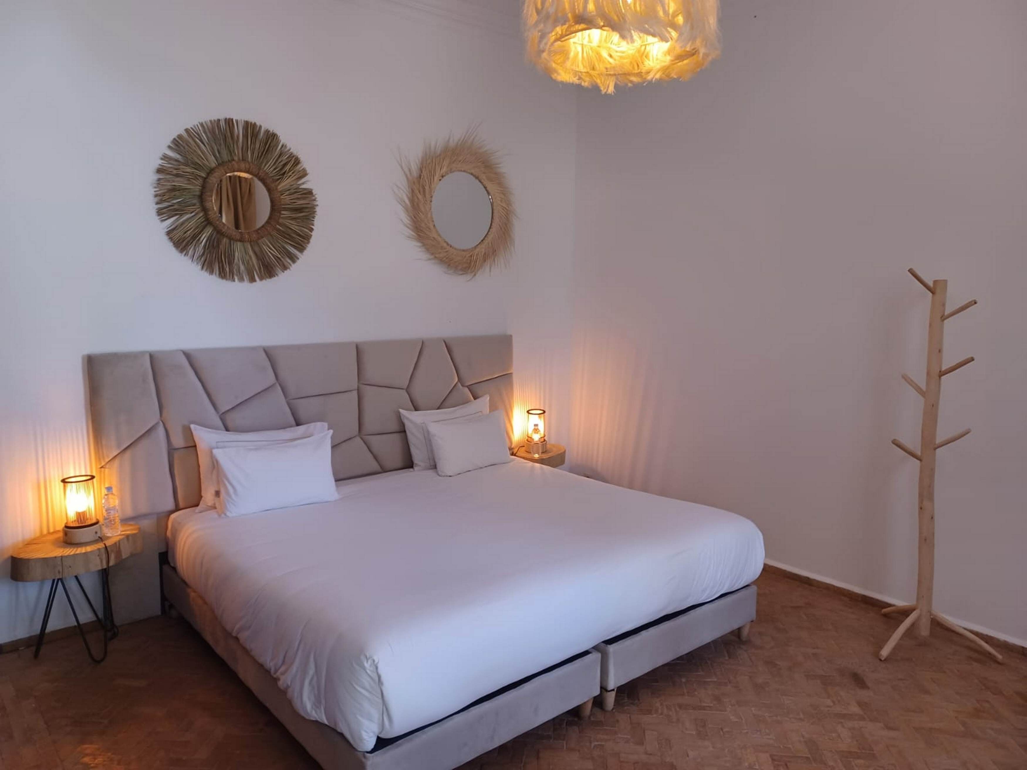 A bedroom with a bed, two bedside tables with lamps, a wooden coat rack, and two wall decorations.