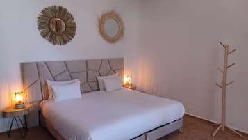 A bedroom with a bed, two bedside tables with lamps, a wooden coat rack, and two wall decorations.