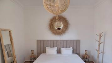 A bedroom with a large bed, a mirror, two bedside tables, a wooden coat rack, and a woven ceiling light fixture.