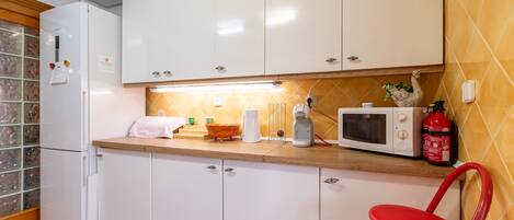 Una cocina con armarios blancos, microondas, tostadora, una silla roja y un extintor.