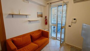 A small, bright room with a sofa, a door leading outside, and a small table.