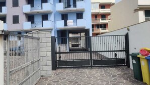 A multi-story residential building with balconies, a gated entrance, and a stone-paved courtyard.