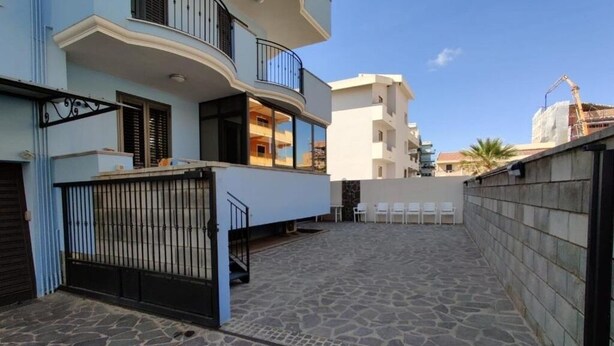 A residential building with a stone-paved courtyard, a gated entrance, and a balcony with a metal railing.