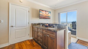 A bathroom with a large vanity, a door, and a view of the ocean through a sliding glass door. - Last-Minute August Beach Deals – Save Big! (Treasure Island)