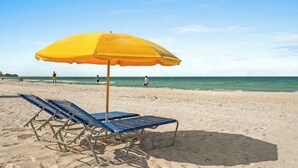 A beach with a yellow umbrella and two blue lounge chairs. - Last-Minute August Beach Deals – Save Big! (Treasure Island)