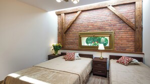 A bedroom with two beds, a brick wall, a window with a view, and a chandelier.
