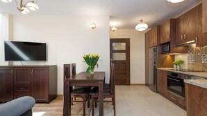 A modern kitchen with wooden cabinets, a dining table with chairs, a flat-screen TV, and a vase with yellow flowers.