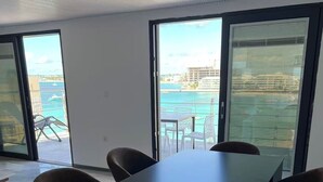 Een moderne kamer met een grote tafel en stoelen, ramen met uitzicht op zee en gebouwen, en een plafond met een uniek patroon.