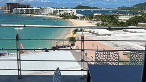 Een balkon met uitzicht op een strand, een cruiseschip en een bergachtig landschap.