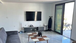 Een moderne woonkamer met een grijze bank, een salontafel en een aan de muur bevestigde televisie.