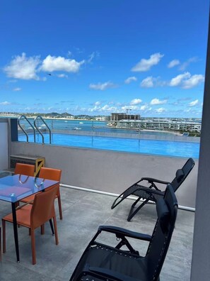 Uma varanda com vista para a piscina, uma mesa com cadeiras e uma espreguiçadeira.