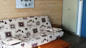 A cozy room with a wooden wall, a sofa with a patterned cover, a small wooden table, and a framed picture above the sofa. - Functional studio for 4, West facing in Valloire (Valloire)