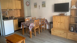 A compact kitchen with wooden cabinets, a dining table with chairs, a small refrigerator, and a television on the wall. - Functional studio for 4, West facing in Valloire (Valloire)