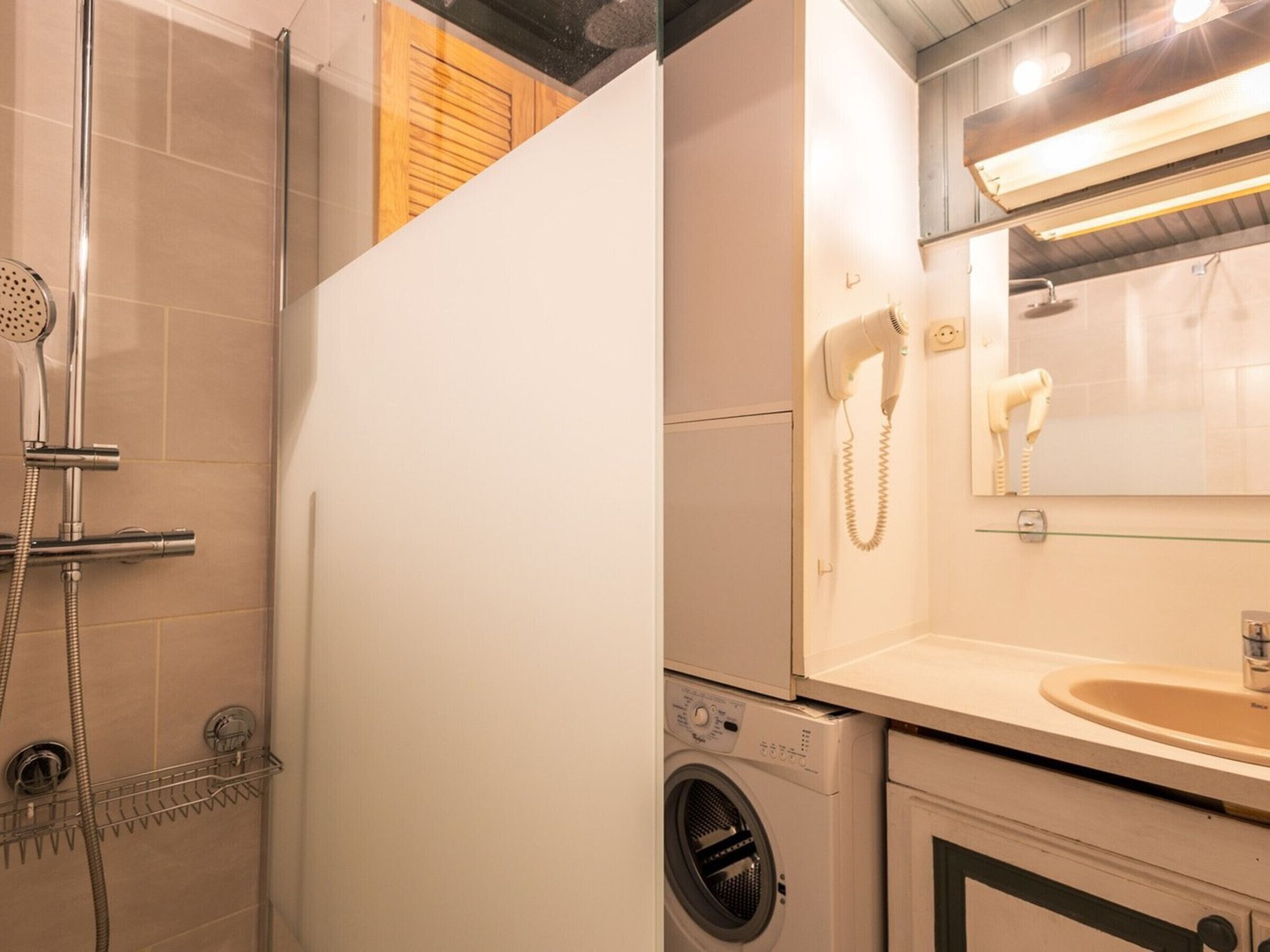 A bathroom with a shower, a hairdryer, a washing machine, and a sink.