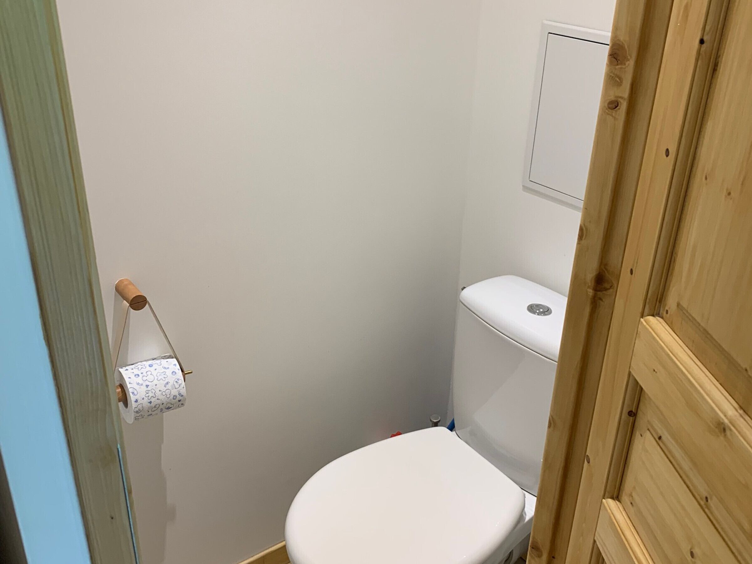 Une petite salle de bain compacte, avec des toilettes blanches, un cadre de porte en bois et un porte-rouleau de papier toilette fixé au mur.