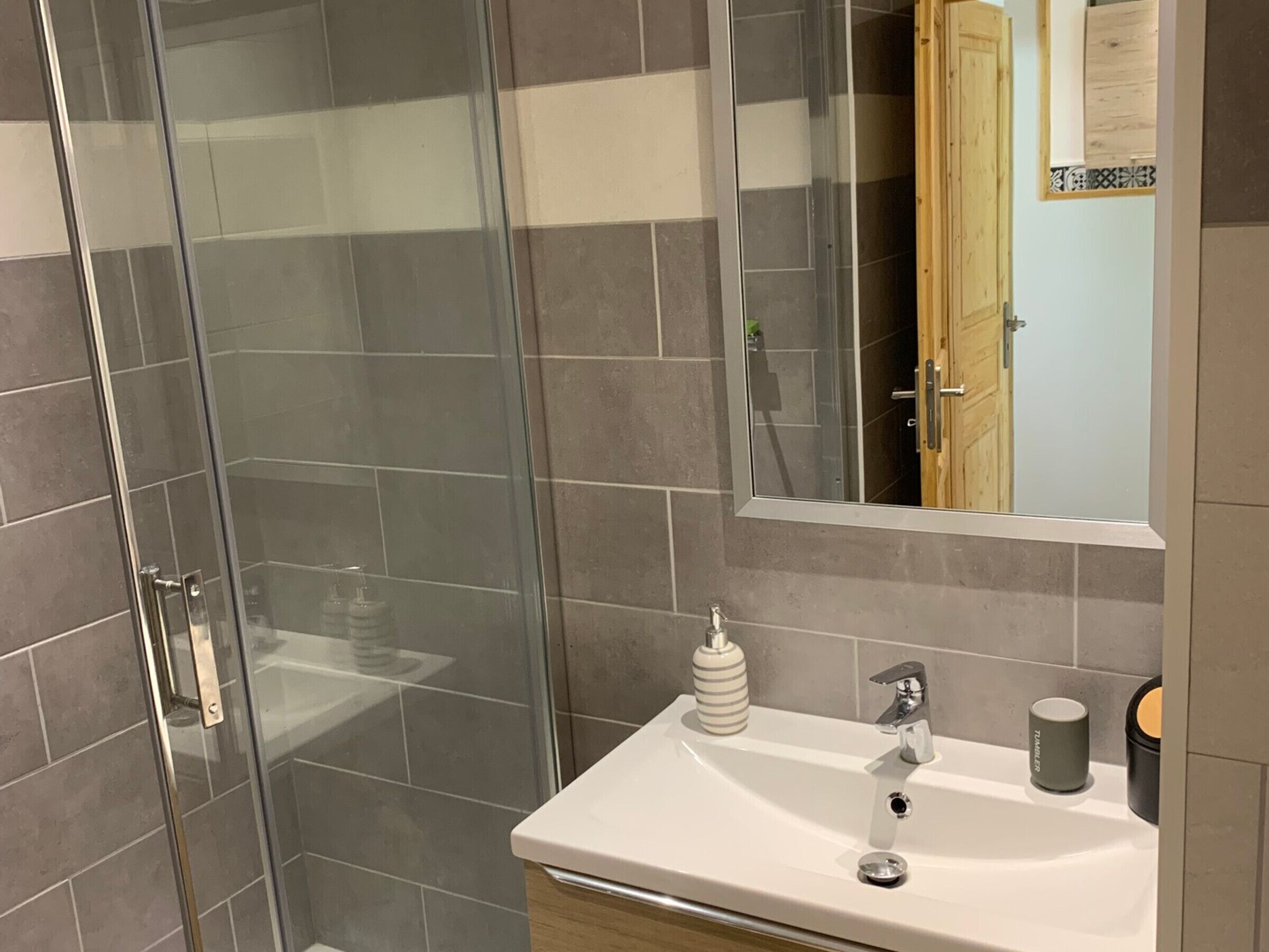 Un baño moderno con cabina de ducha de vidrio, un lavabo blanco con grifo cromado y un mueble de madera debajo.