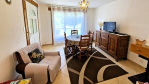 A living room with a sofa, dining table, chairs, a TV on a wooden cabinet, and a chandelier. - Charming holiday home in Chauffayer - 4 pers - Aubessagne (Aubessagne)
