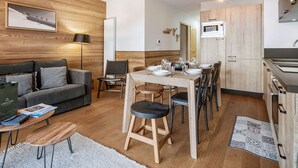 A modern living room with a sofa, a dining table set for four, and a kitchen area with wooden cabinets and a microwave. - 2BR Apartment in Les Saisies, sleeps 6 (Les Saisies)