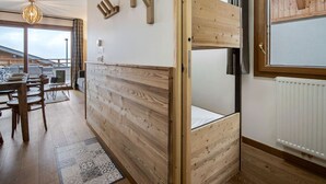 A modern room with a bunk bed, wooden wall decor, a dining area with a table and chairs, and a view through a large window. - 2BR Apartment in Les Saisies, sleeps 6 (Les Saisies)
