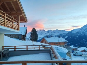 Een houten chalet met een sneeuwbedekte veranda met uitzicht op een bergachtig landschap.