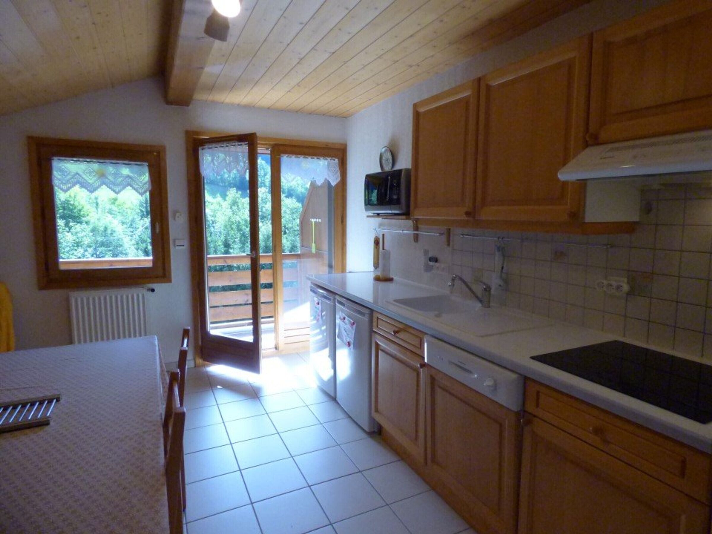A kitchen with wooden cabinets, a microwave, a sink, and a window overlooking a balcony.