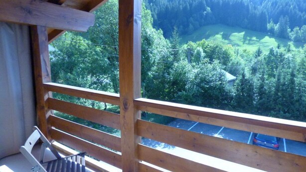 A balcony with a wooden railing overlooking a forested valley.