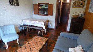 Un salon chaleureux avec un canapé bleu, un fauteuil assorti, une table basse en bois et une table à manger recouverte d’une nappe à motifs.