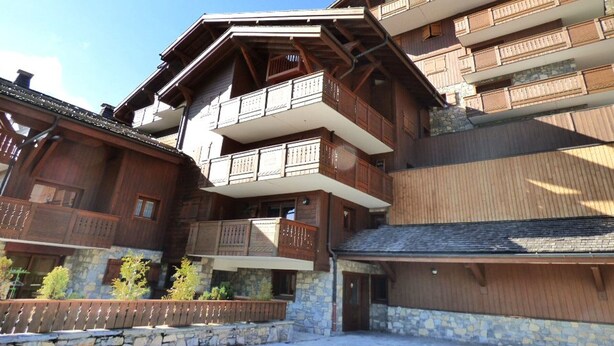 Un bâtiment en bois à plusieurs étages, doté de balcons, de fondations en pierre et d’un toit en pente.