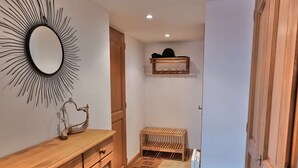 Un couloir avec une commode en bois, un miroir orné d’un motif en forme de soleil, un petit banc et un radiateur.
