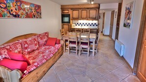 Un salon chaleureux avec un canapé en bois, une table à manger avec des chaises et un coin cuisine doté de meubles en bois et d’un dosseret carrelé.