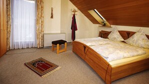 A bedroom with a wooden bed, a small bench, a ceiling light, and a window with curtains. - Apartment 'Margot Armbruster' with Mountain View, Balcony and Wi-Fi (Bad Rippoldsau-Schapbach)