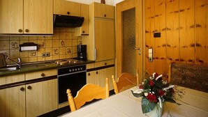 A kitchen with wooden cabinets, a stove, and a dining table with a vase of flowers. - Apartment 'Margot Armbruster' with Mountain View, Balcony and Wi-Fi (Bad Rippoldsau-Schapbach)
